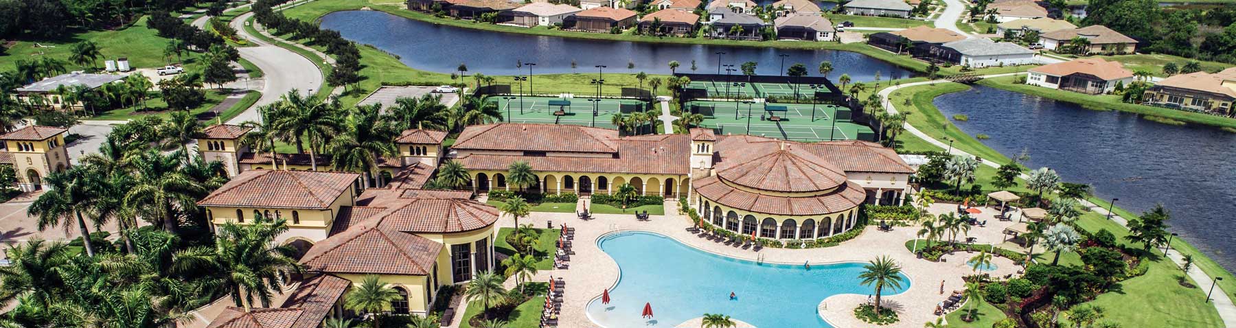 Aerial view of a luxury community with a large resort-style pool, clubhouse, tennis courts, playground, and surrounding lakes and homes.