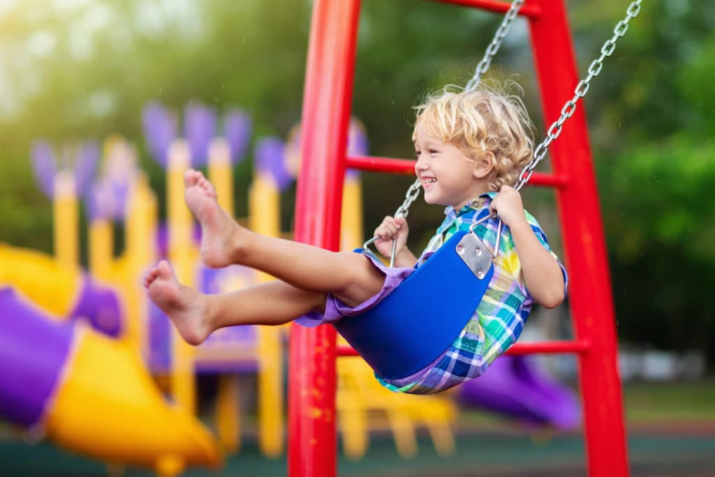A child playing on a swing at a colorful outdoor playground at the Primrose School at Wellen Park