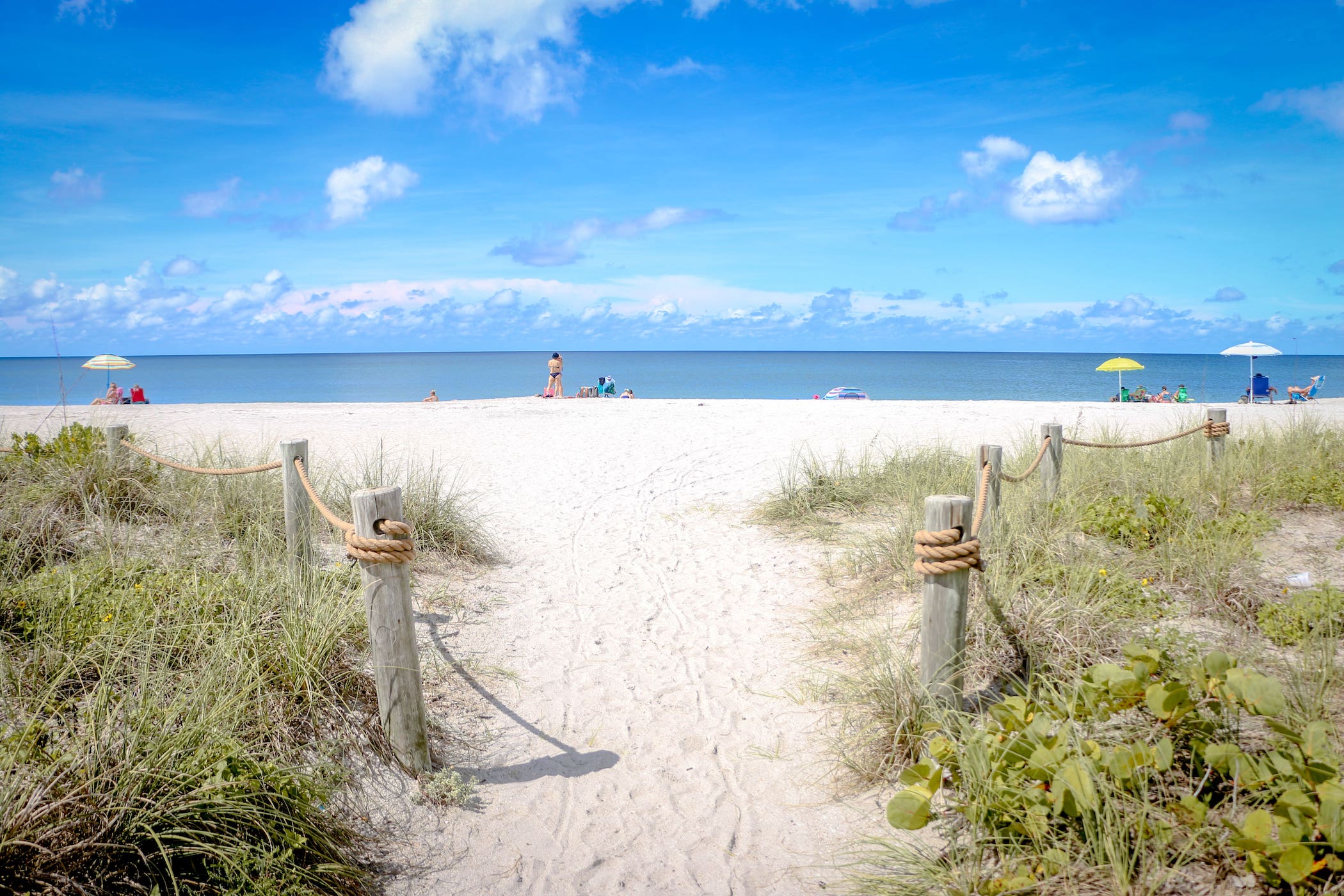 The exit of a sand pathway surrounded by shrubs, leading to the beach thats