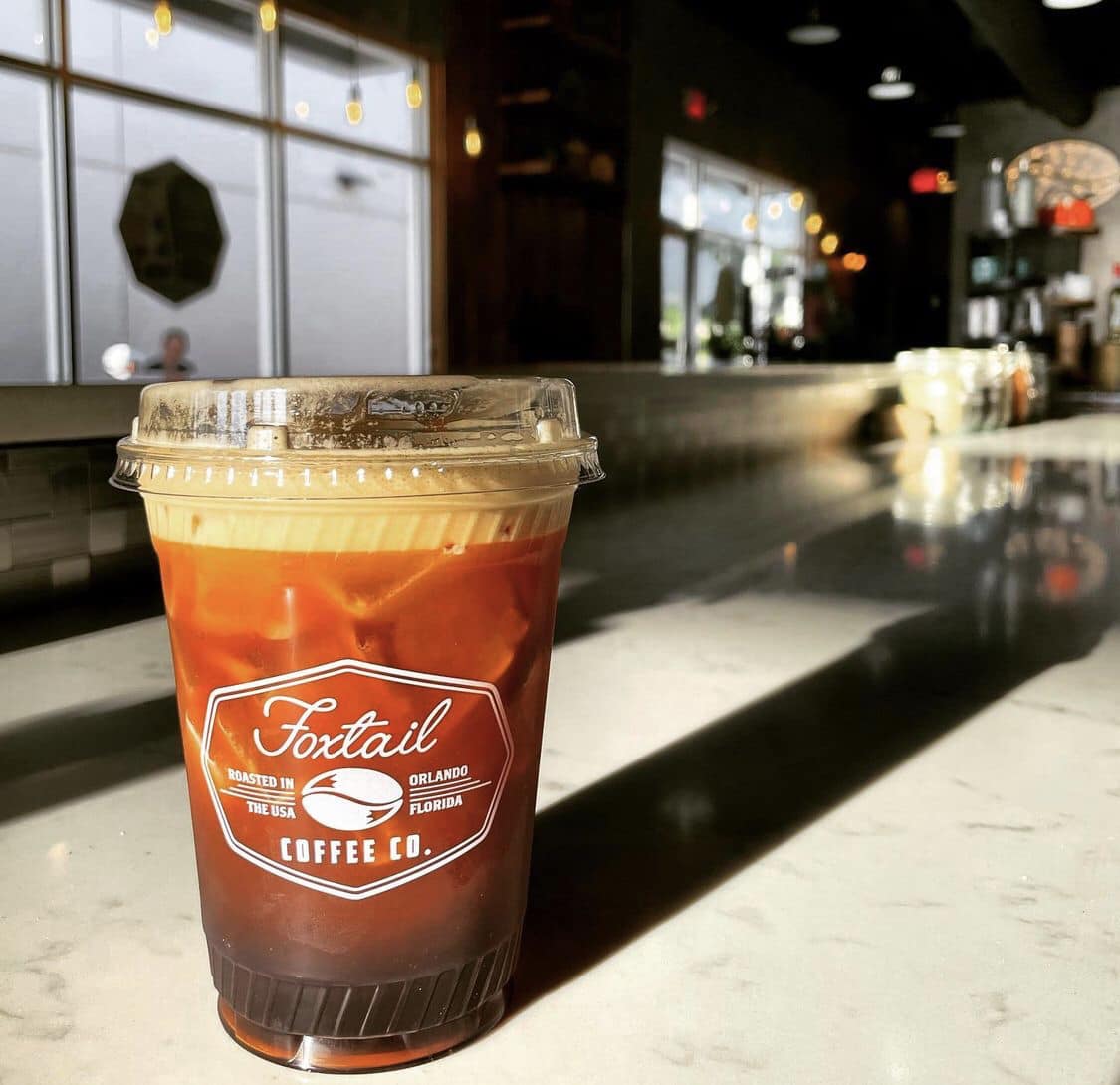 An iced balck coffee drink topped with foam in a clear to-go cup from the Foxtail Coffee cafe in Downtown Wellen