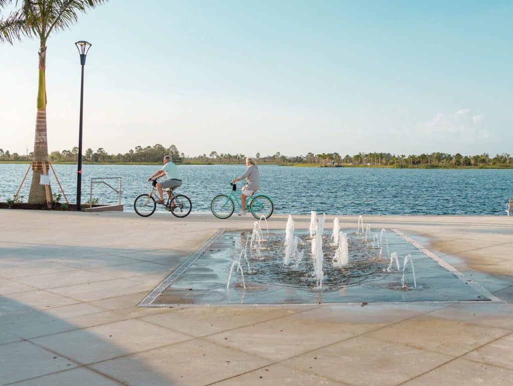An open clearing with a water pad, and the lake in the background with people riding their bikes along the waterfront