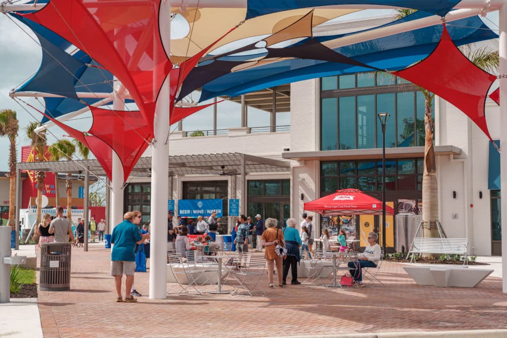 A group of people outside under shade in front of stores
