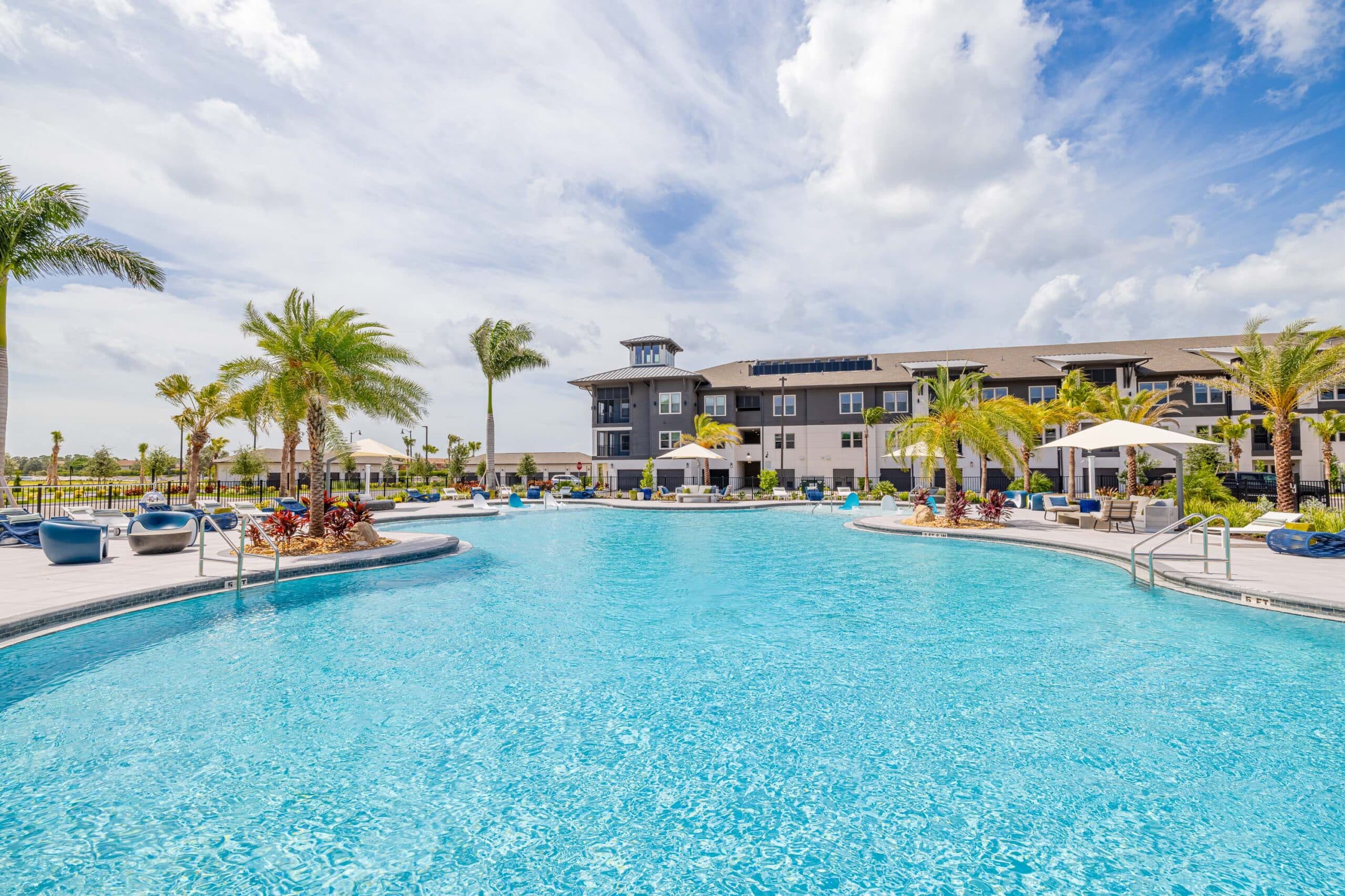 A curved pool surrounded by pool chairs and palm trees