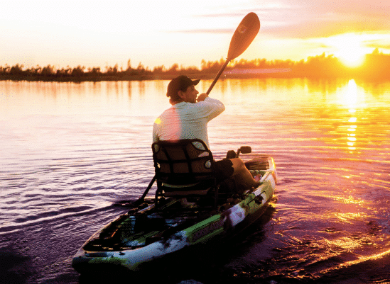 A man riding a kayak in water thats reflecting the sunset