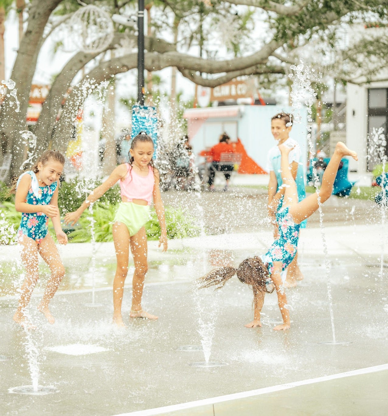 Children in swimsuits playing on a splashpad with parents sitting out of the splasho zone