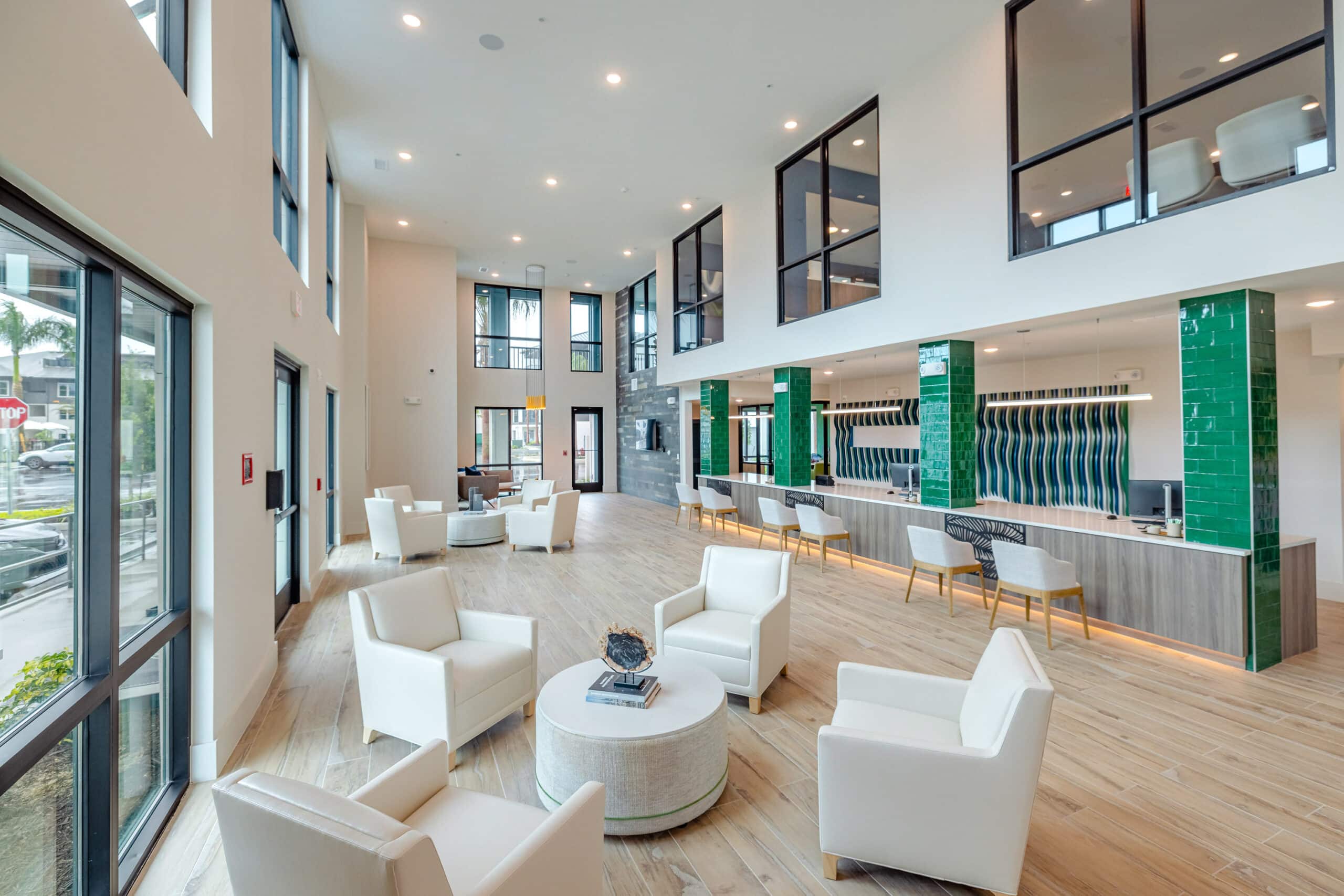 A reception with white chairs, green pillars and multiple front desk spots