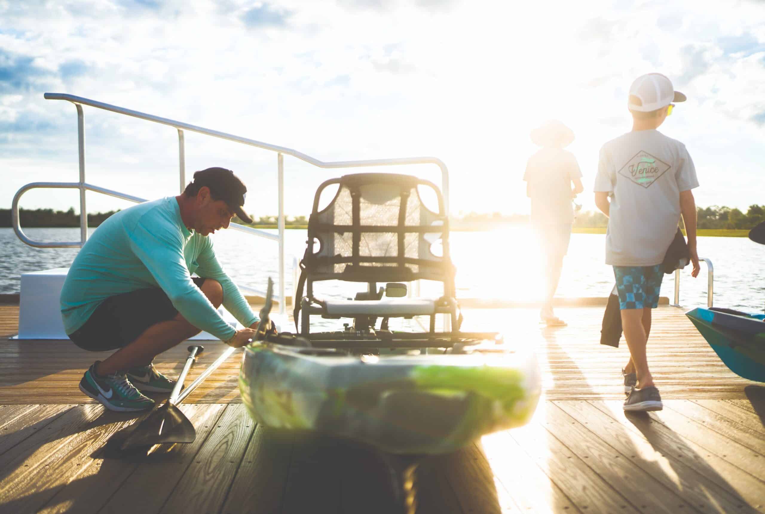 A man setting up a small boat while two children walk closer to the edge of the boat dock in the suns light