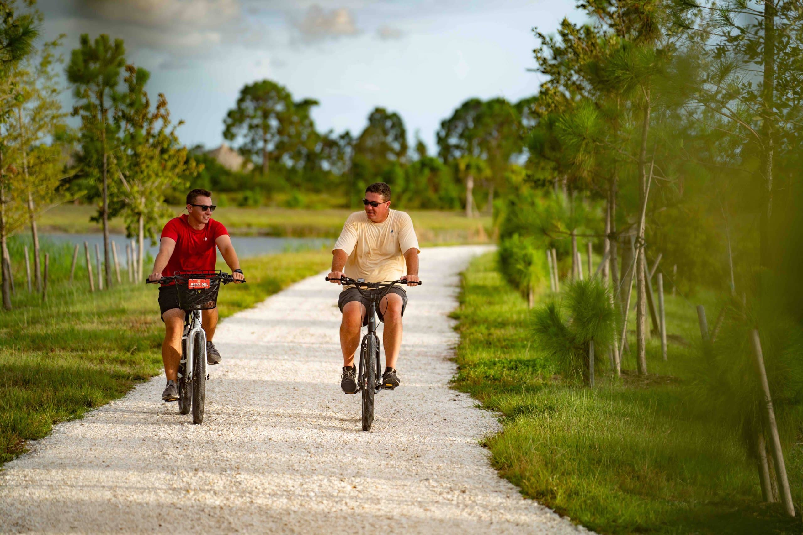 Two people riding their bikes on a trail thats right by the water and surrounded by greenery