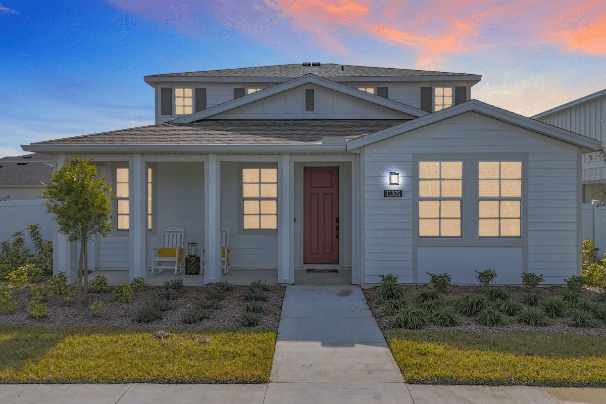 A single family home with two stories, its lights turned on and a manicured lawn out front in the early evening