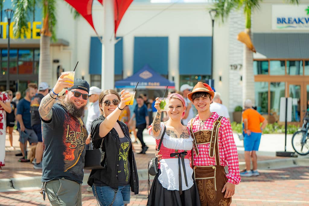 Four holding up their drinks and smiling celebrating Oktoberfest in the middle of Downtown Wellen Park