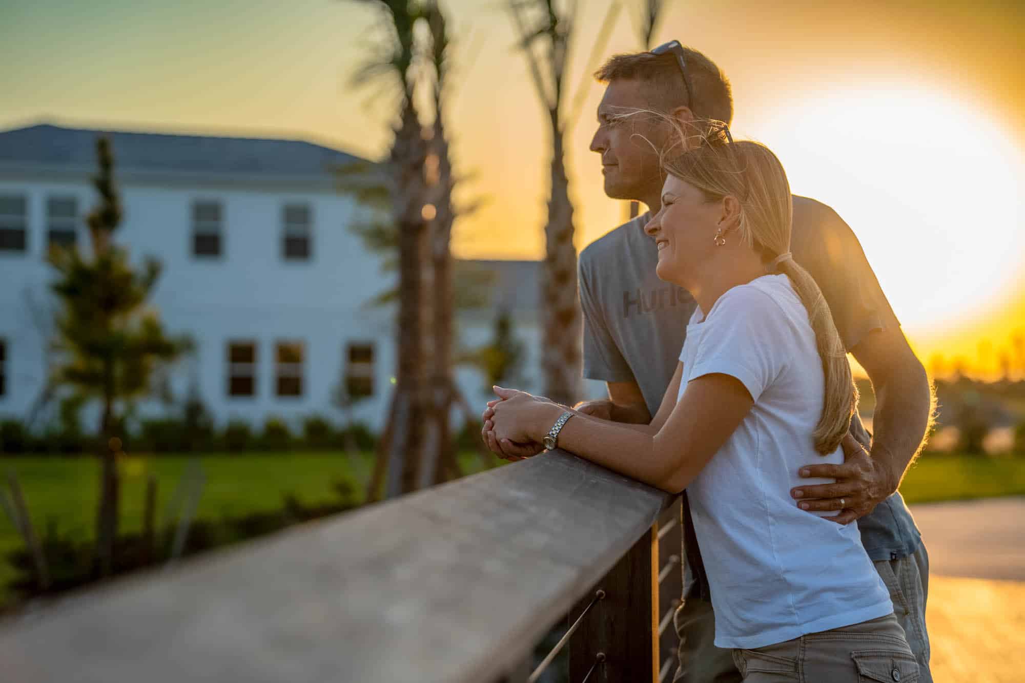 A couple looking over a wooden bridge with the sunset as and Wellen Park houses as the backdrop
