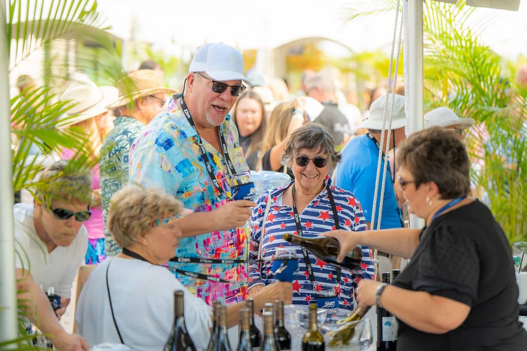 A group of seniors standing in front of a table with bottles of wine and getting their glasses refilled
