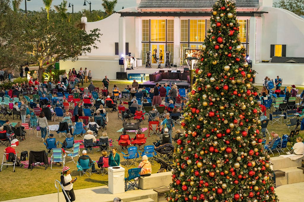Several people seated in lawn chairs in front of a stage, with a large christmas tree behind them