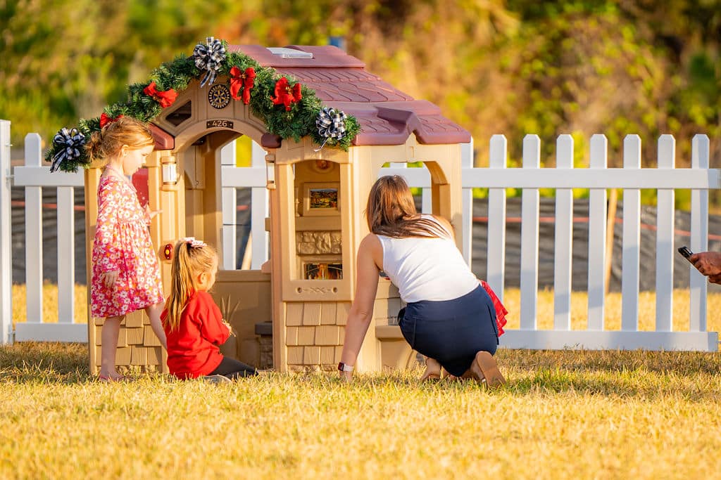 Two little girls and a woman playing with a childrens playhouse with christmas decoration on it